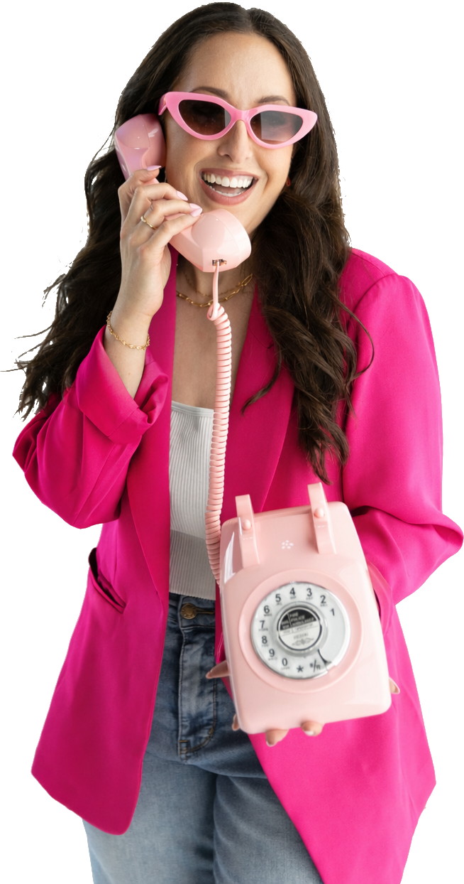 A smiling young woman in a pink blazer talking on a pink telephone